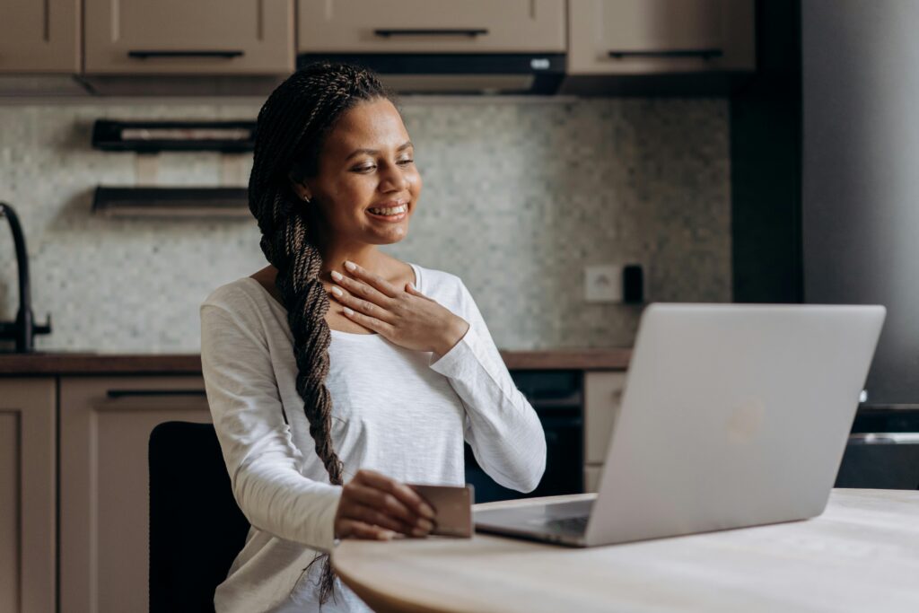 Smiling woman using laptop for online shopping with credit card in hand.